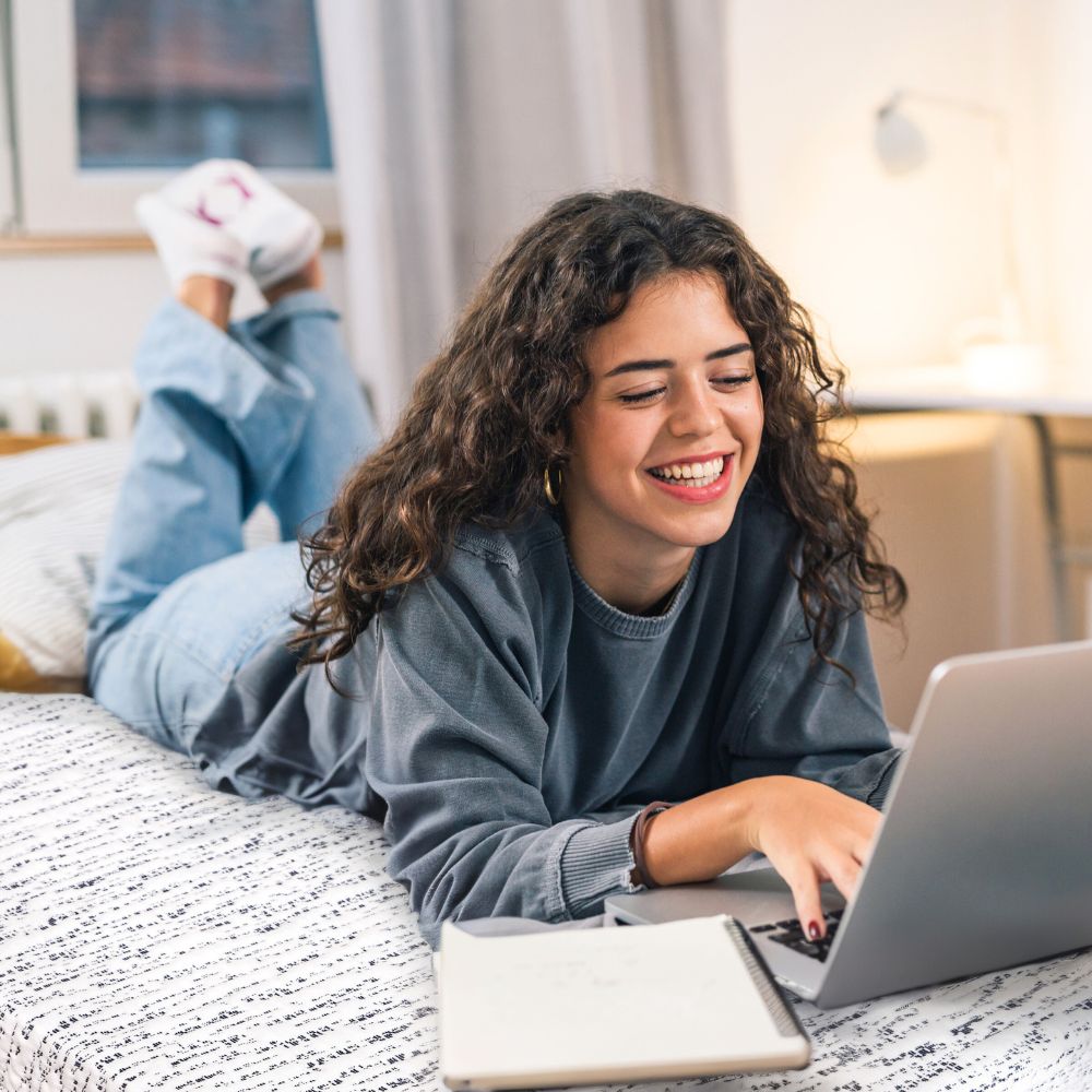 Student typing on top of mattress topper in college dorm